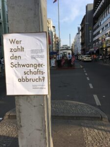 Plakataktion vom What the Fuck-Bündnis zu der Frage, wer eine Abtreibung zahlen muss. Hängt am Check-Point Charlie.
