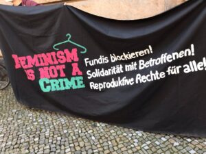 Foto von schwarzem Transpi mit der bunten Aufschrift: feminism is not a crime