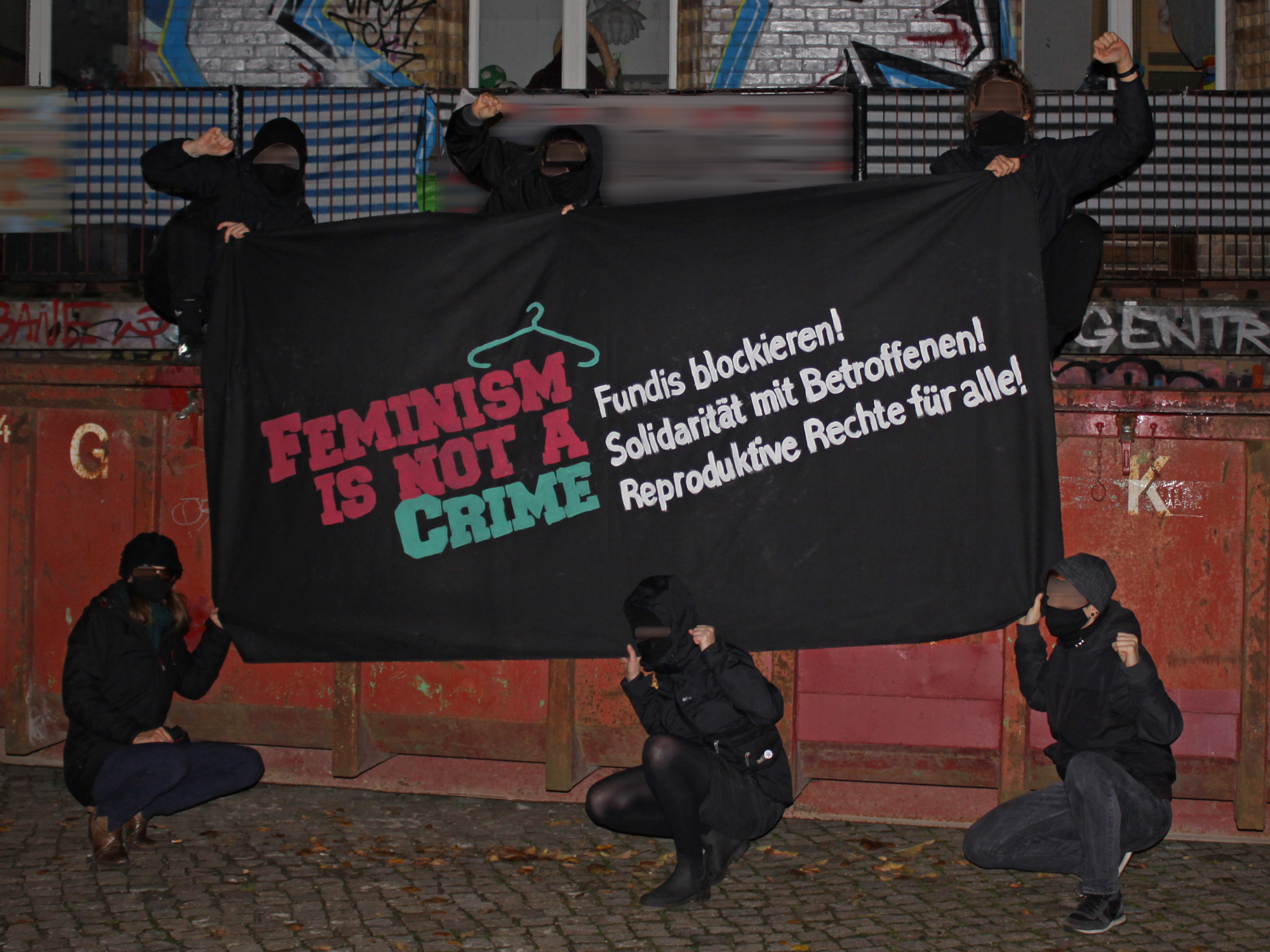Foto mit Aktivist:innen und Transpi mit der Aufschrift "Feminism is not a crime"