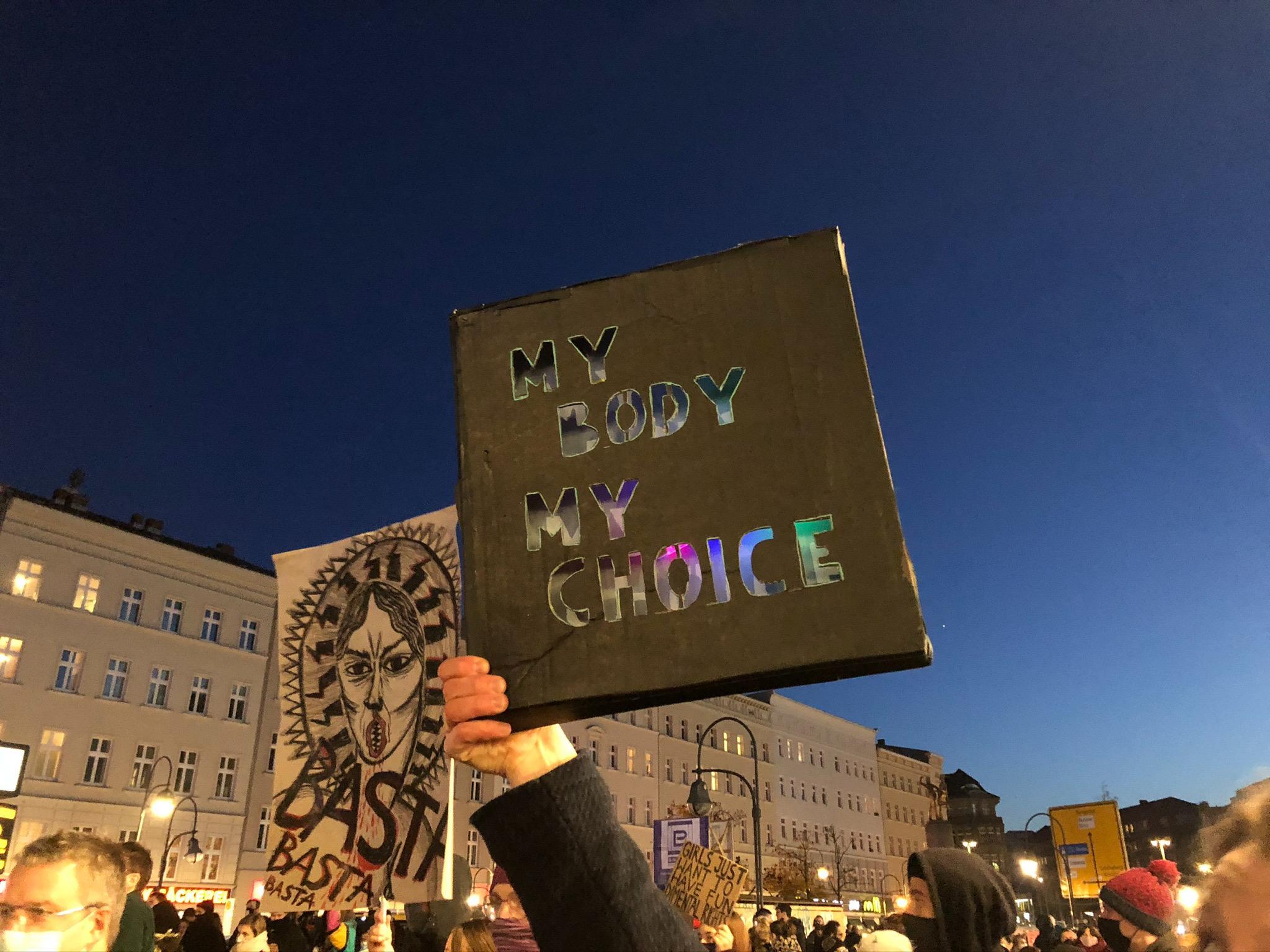 Foto. Ein Arm hält ein Schild hoch, auf diesem steht: My Body my Choice.